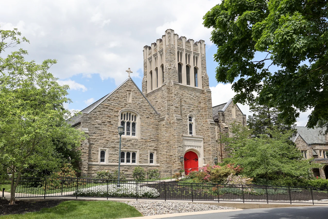 1W8A3842 Exterior of stone church surrounded by trees and gardens.