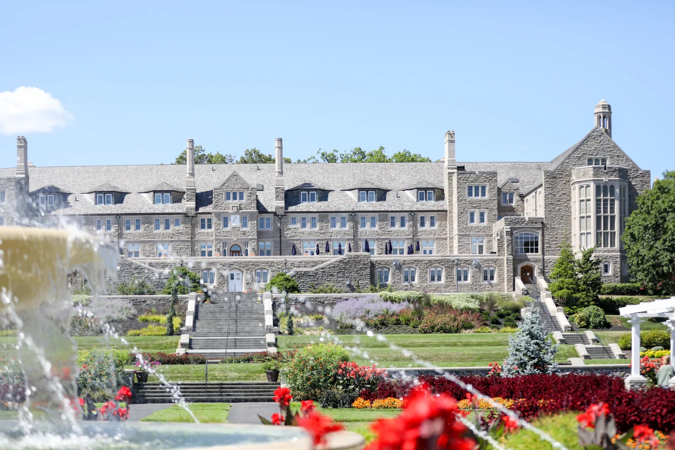 2V9A0253 Sprawling stone building framed by gardens and a fountain in the foreground.