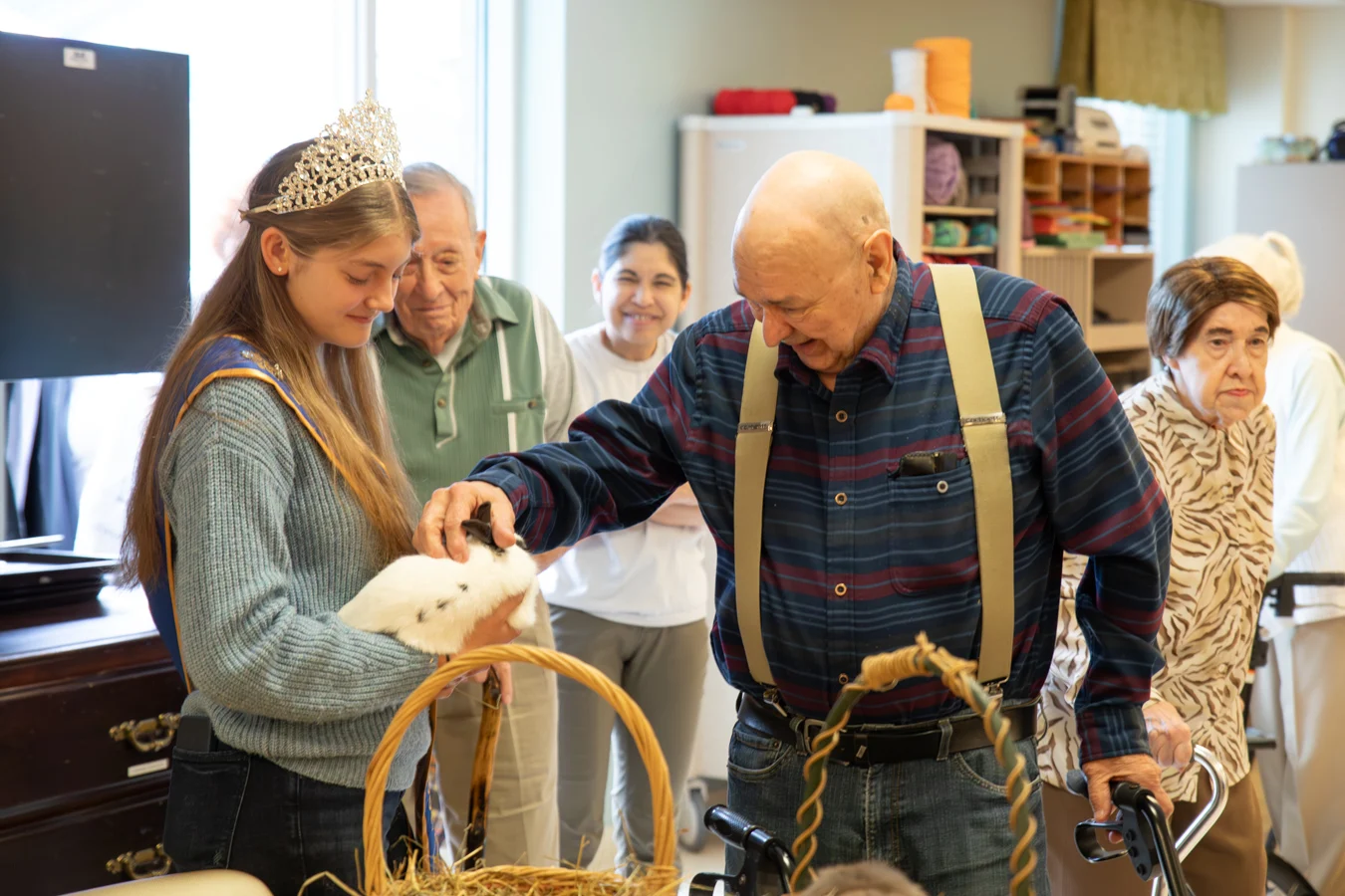 Volunteer holding out a bunny while a smiling senior man pets the bunny's ears.