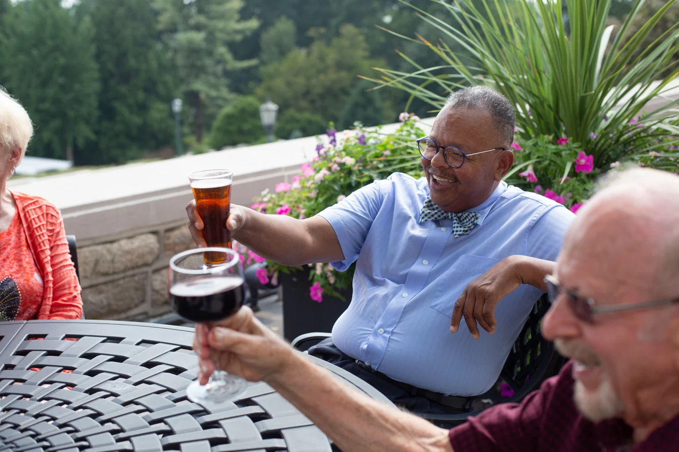 Smiling seniors seated outdoors and raising their glasses up.